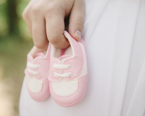A close-up of a hand holding pink baby shoes, symbolizing new life and parenthood.