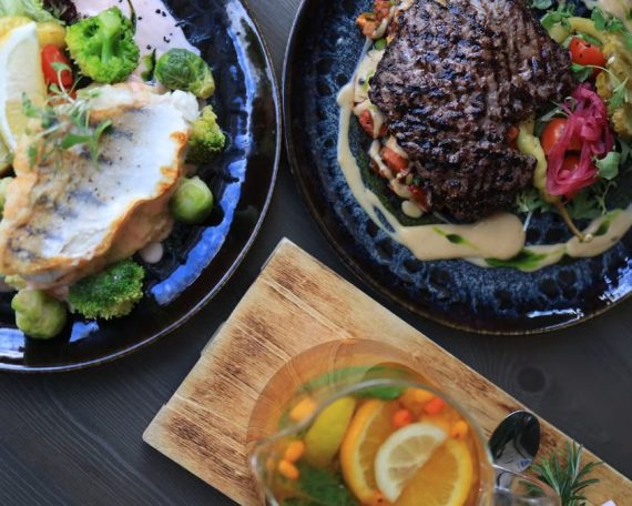 Top view of gourmet fish and steak dishes with fresh citrus and herbs on a stylish table setting.